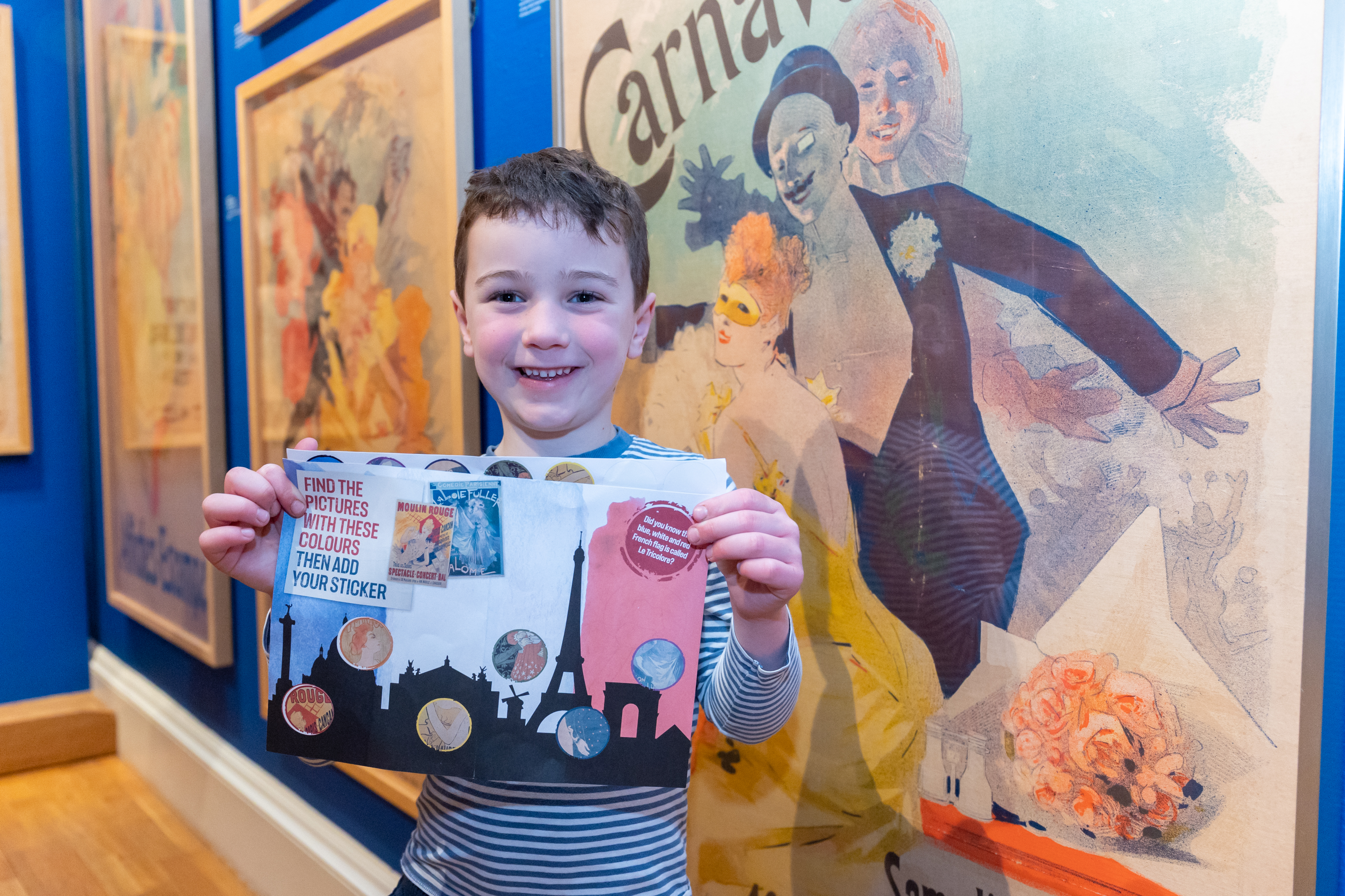 A child holds an activity trail in front of artwork