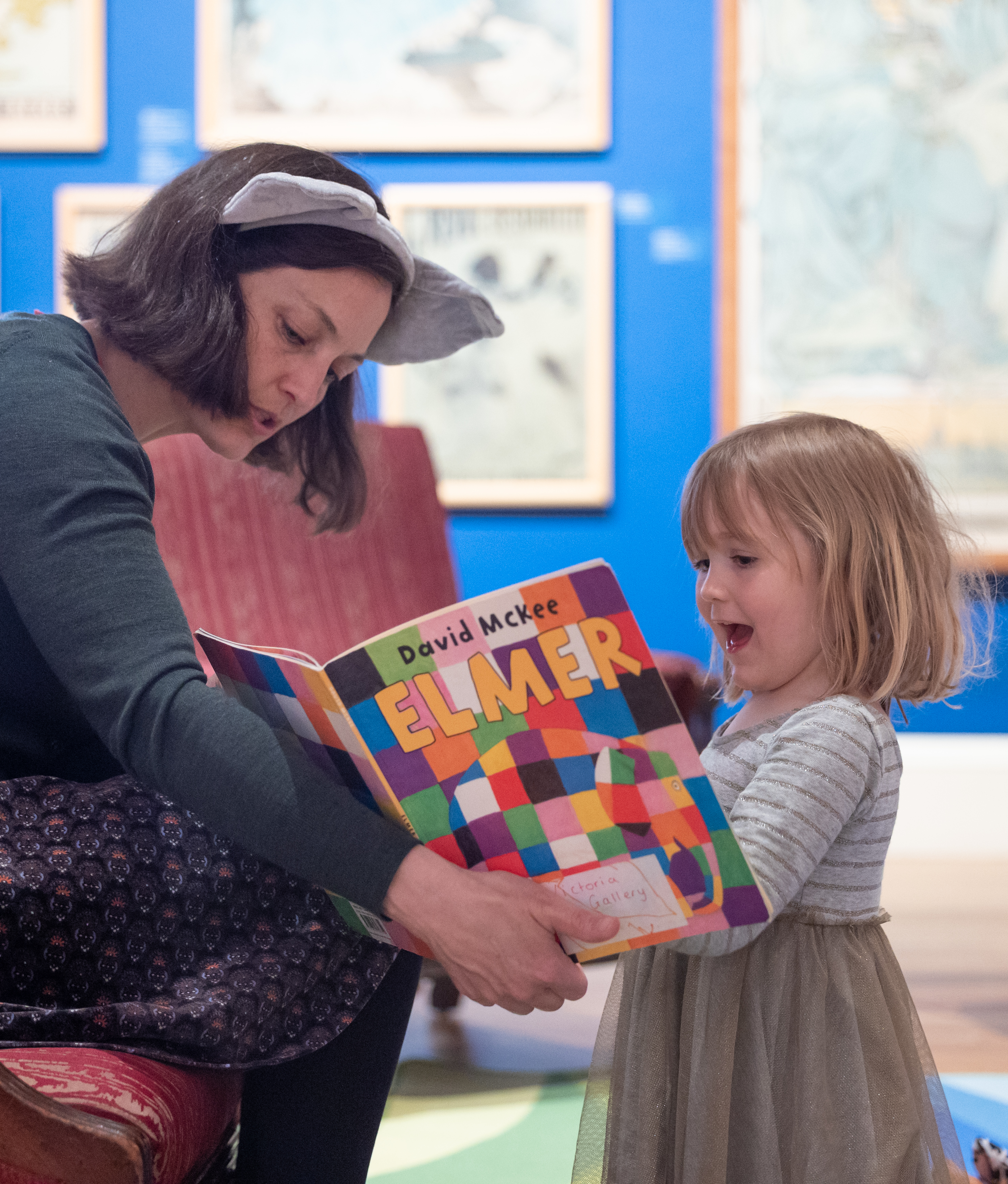 a woman reading  Elmer the Elephant book to a young girl in an art gallery