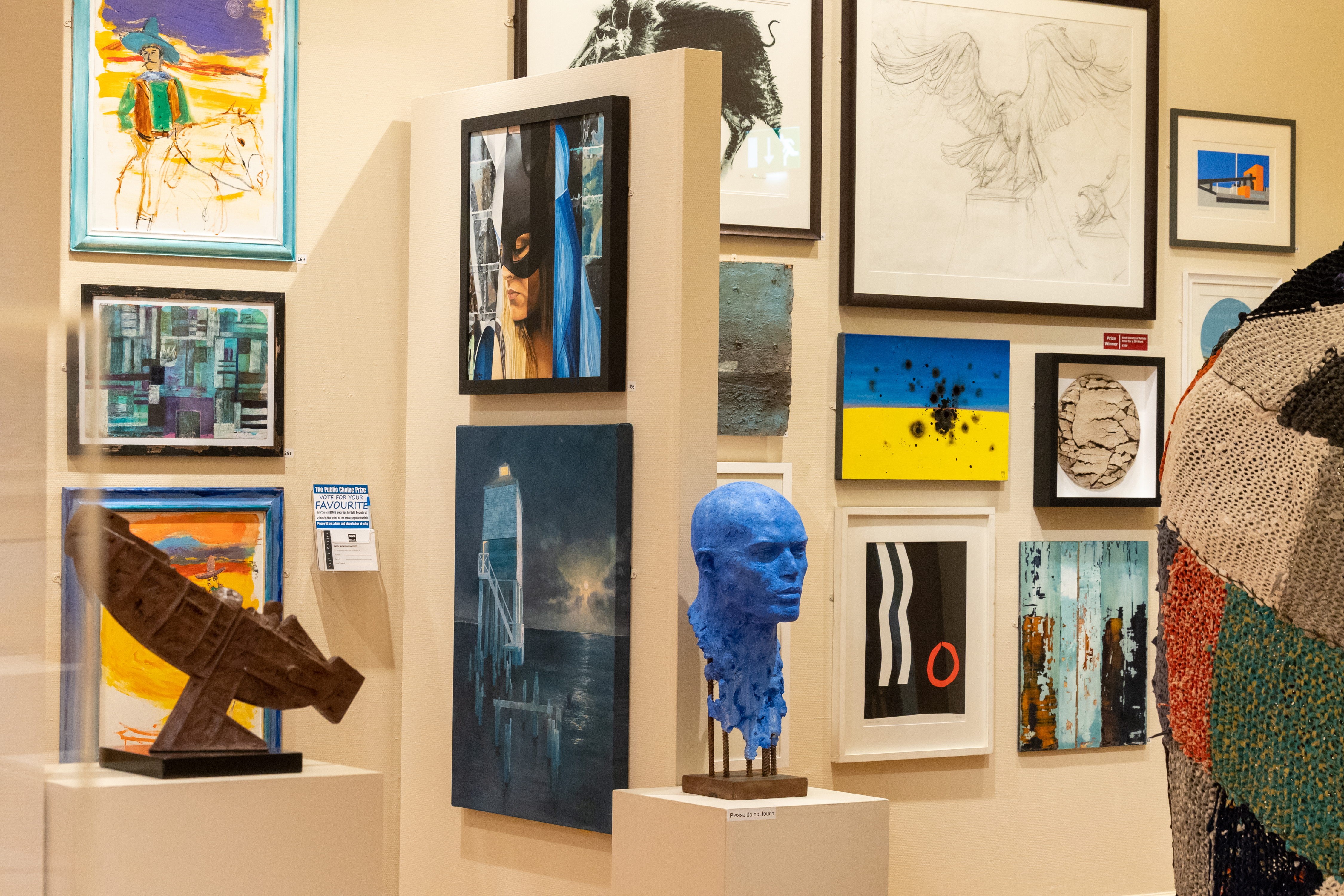 A photo of Bath Society of Artists exhibition in 2023, showing paintings on the wall with sculpture in the foreground.