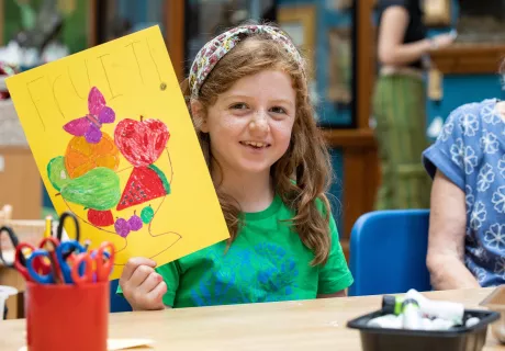 A child holding up a piece of artwork that she has made.