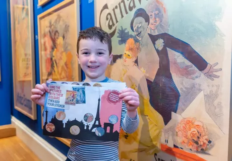 A child holds an activity trail in front of artwork