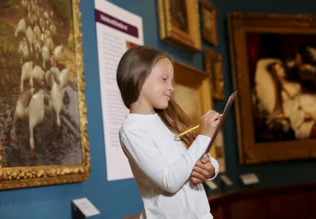 A girl with a clipboard in the gallery, which has blue walls and a painting of geese on the wall